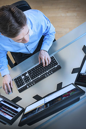 men typing on a keyboard with three monitors
